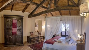 A bedroom with a wooden ceiling, a bed with a canopy, a wardrobe, and a small table with a lamp. - Agriturismo Fattoria La Prugnola (Montescudaio)