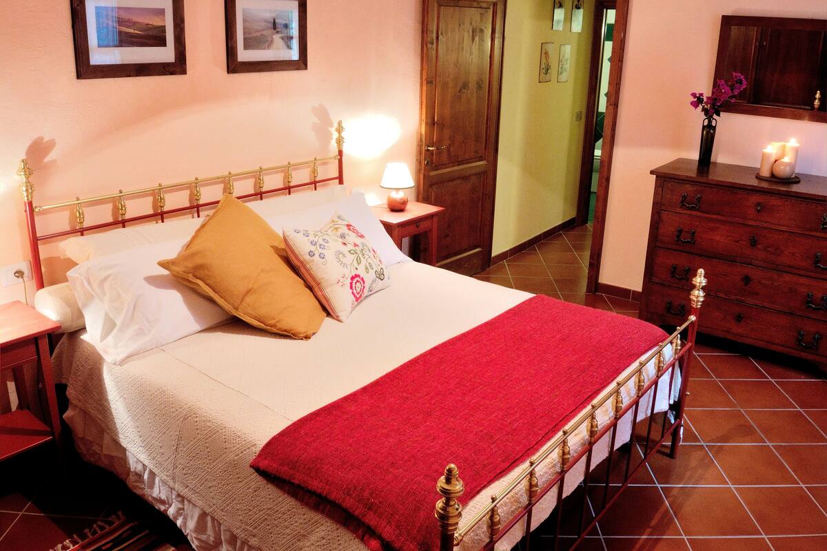 A neatly made bed with a red blanket, a wooden headboard, and two bedside lamps.