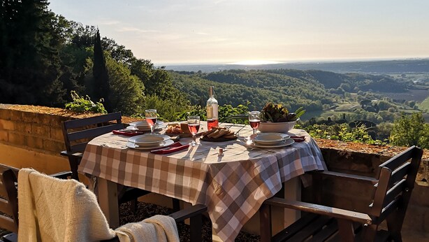An outdoor dining table set with plates, glasses, and a bowl of salad, overlooking a scenic landscape. - Agriturismo Fattoria La Prugnola (Montescudaio)
