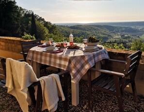 An outdoor dining table set with plates, glasses, and a bowl of salad, overlooking a scenic landscape. - Agriturismo Fattoria La Prugnola (Montescudaio)