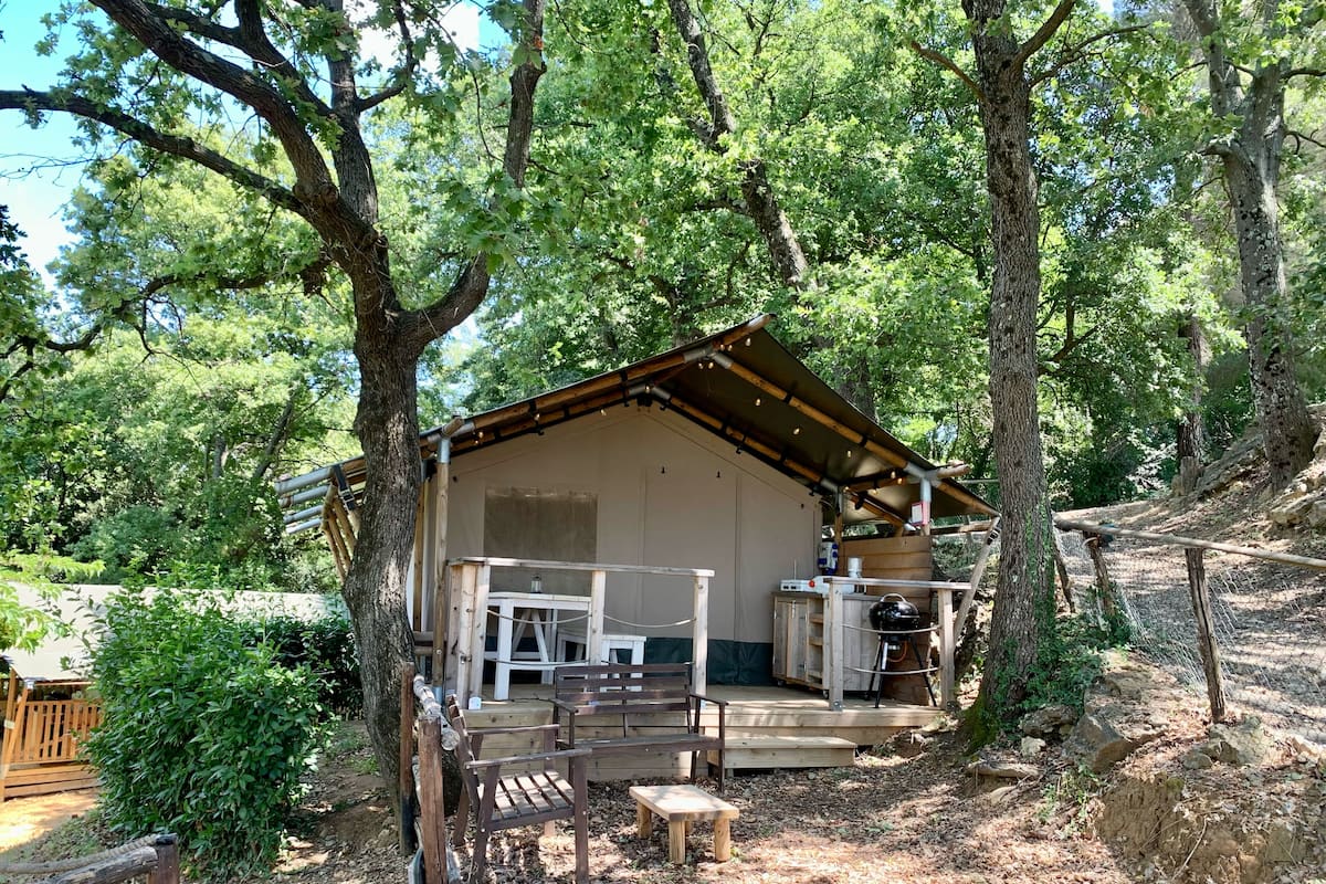A rustic cabin with a wooden deck, a bench, and a table.