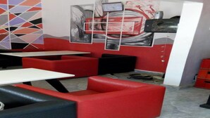 Een moderne lounge met rode en zwarte zitplaatsen, witte tafels en abstracte wanddecoratie.