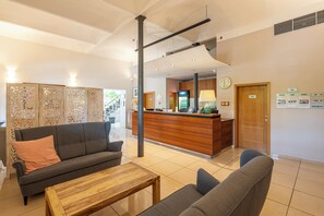 A reception area with a wooden reception desk, a grey sofa, and a coffee table. - Hotel Chvalska Tvrz (Prague)