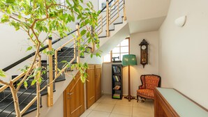 Eine Treppe mit Holzgeländer, eine grüne Stehlampe, eine Vintage-Uhr, ein Bücherregal und ein gemustertes Sessel.