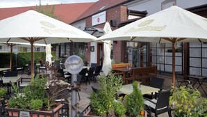 An outdoor seating area with tables and chairs under umbrellas, surrounded by potted plants.
