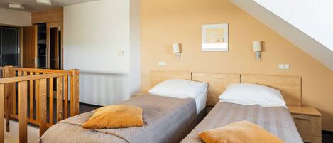 A room with two beds, a wooden headboard, a nightstand, a wall-mounted lamp, and a framed picture.