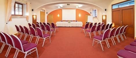 A conference room with rows of purple chairs, a white table, and a projector screen.