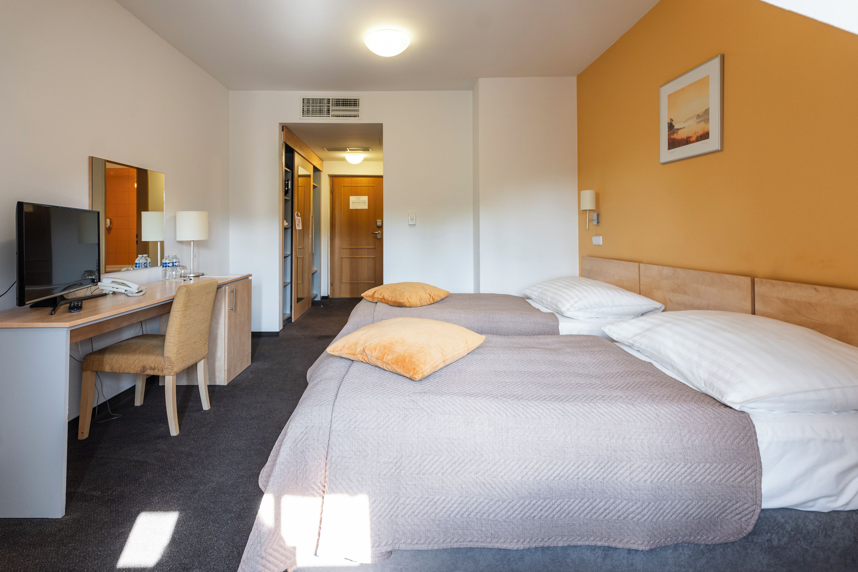 Quarto de hotel com escrivaninha, duas camas, televisão e um quadro na parede.