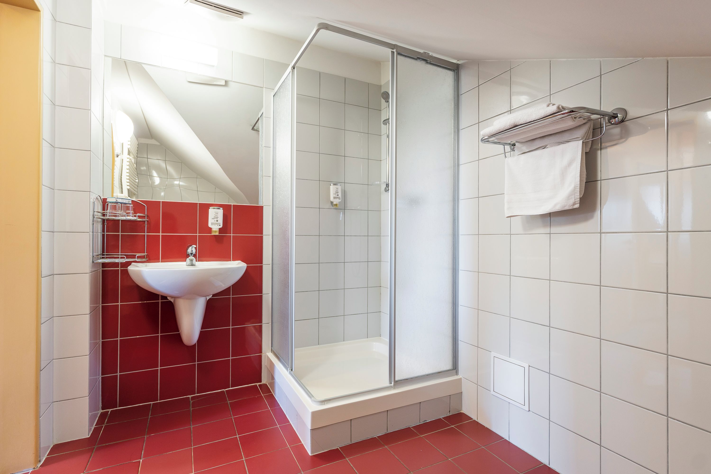 Un baño con cabina de ducha de vidrio, lavabo blanco y paredes con azulejos rojos.