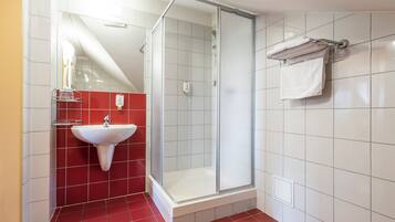Un baño con cabina de ducha de vidrio, lavabo blanco y paredes con azulejos rojos.