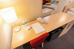 A hotel room with a wooden desk, a lamp, a telephone, a water bottle, a glass, and a red towel. - Hotel Chvalska Tvrz (Prague)