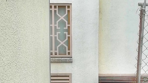 A metal gate with decorative elements, a window with a geometric pattern, and a wall with a textured surface.