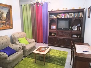 Una sala de estar con un sofá, una mesa de centro, un televisor y una estantería.