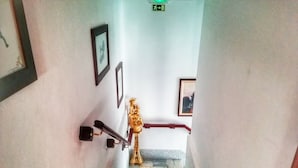 A staircase with a handrail, a wall-mounted emergency exit sign, and framed pictures.