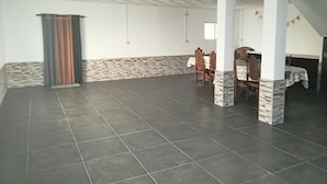 A spacious room with a tiled floor, a dining area with chairs and a table, and a bed with a patterned bedspread.