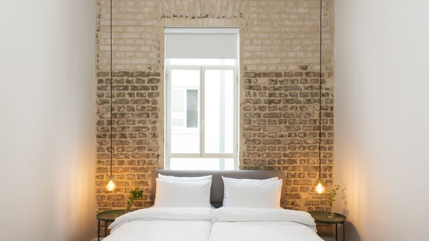 Ein Schlafzimmer mit Backsteinwand, einem Fenster, einem Bett mit weißer Bettwäsche und zwei Nachttischen mit Lampen.
