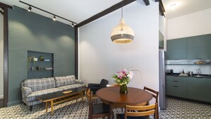 Ein modernes Wohnzimmer mit einer Couch, einem Couchtisch und einem Esstisch mit Stühlen. Es gibt eine Küchenzeile mit Schränken und einem Spülbecken.