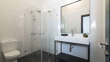 A modern bathroom with a glass-enclosed shower, a white toilet, and a black vanity with a mirror above it.