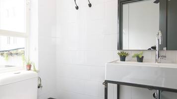 Un baño moderno con inodoro blanco, lavamanos negro y espejo encima. Hay dos pequeñas macetas con plantas en la encimera del lavamanos.