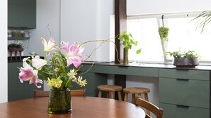 Ein Esstisch mit einer Blumenvase, Holzstühlen und einer grünen Küchenarbeitsplatte mit Schränken und Barhocker.