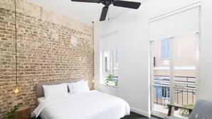 Ein Schlafzimmer mit Backsteinwand, einem Bett, einem Deckenventilator und Blick auf den Balkon.