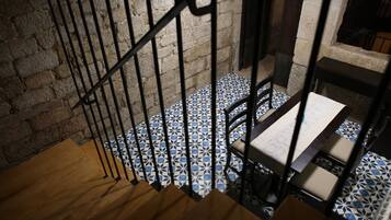 Un escalier doté d’une main courante en bois et d’une rampe en métal, menant à une pièce dont le sol est recouvert de carreaux décoratifs et qui contient une table recouverte d’une nappe blanche.