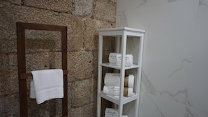 A bathroom with a stone wall, a wooden towel rack, and a white shelf with neatly folded towels. - Muralha Charm House (Lamego)