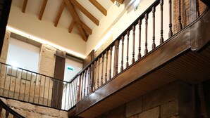 A spiral staircase with wooden steps and metal railings, leading to a second floor with a stone wall and wooden beams. - Muralha Charm House (Lamego)
