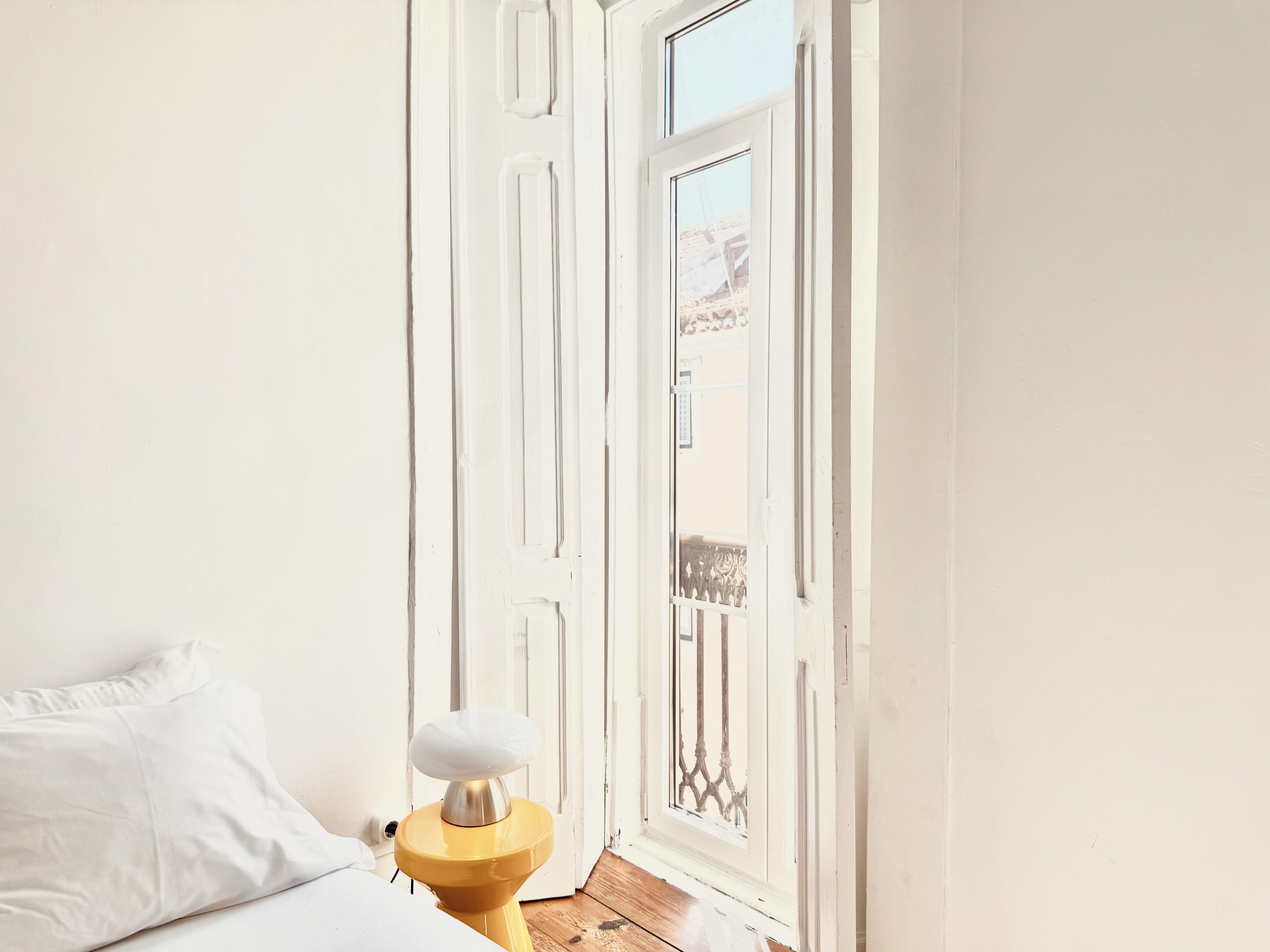 A room with a bed, a bedside table with a lamp, and a door leading to an outdoor balcony.