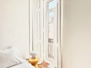 Une chambre avec un lit, une table de chevet avec une lampe et une porte donnant sur un balcon extérieur.