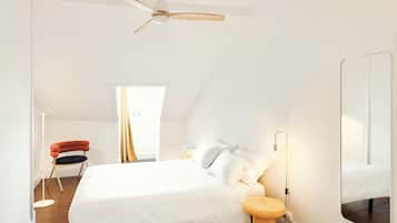 A bedroom with a bed, a bedside table, a mirror, a ceiling fan, and a window with curtains.