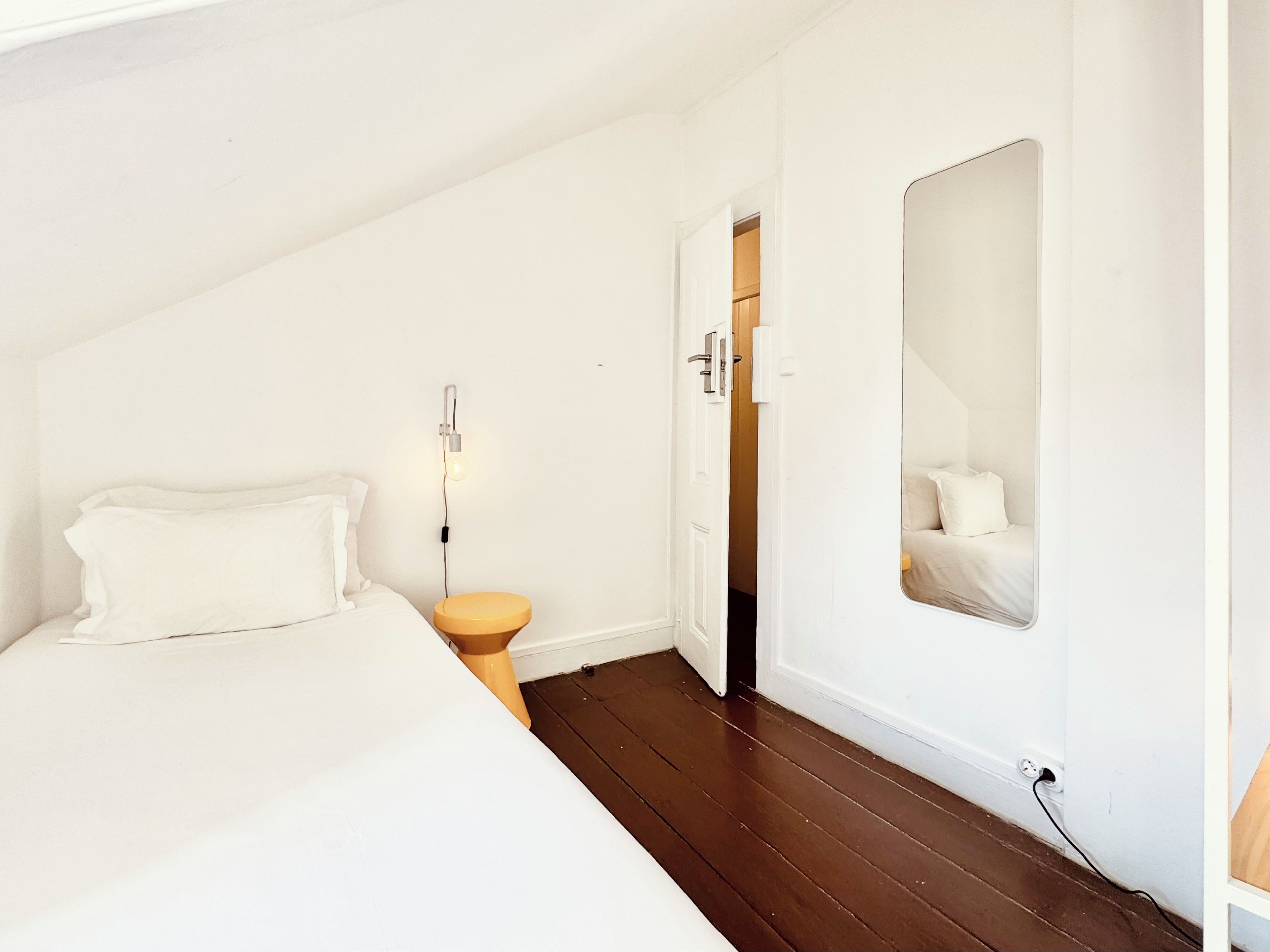 A bedroom with a bed, bedside table, and a mirror on the wall.