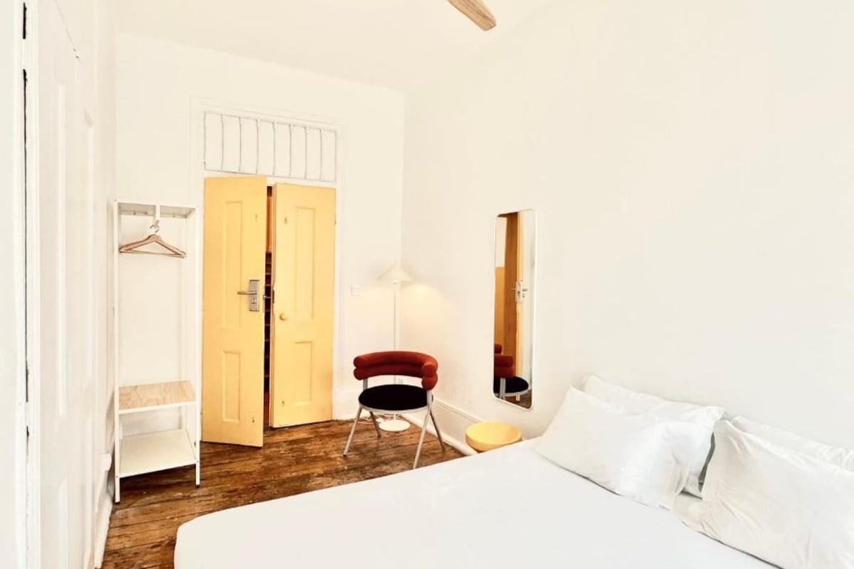 Une chambre d’hôtel avec un lit, une chaise, une armoire, un miroir et un ventilateur de plafond.