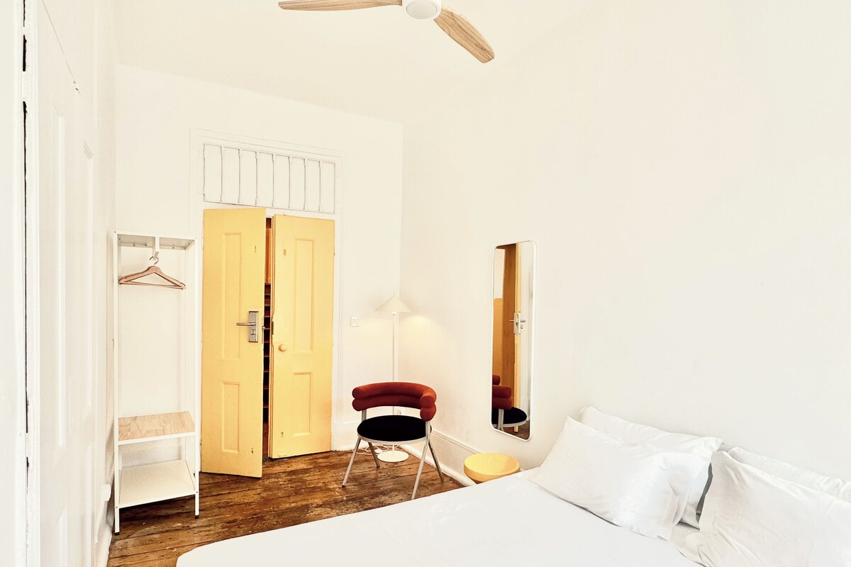 Une chambre à coucher comprenant un lit, une chaise, une armoire, un miroir et un ventilateur de plafond.