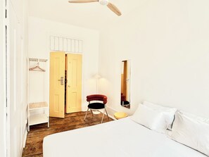 Une chambre à coucher comprenant un lit, une chaise, une armoire, un miroir et un ventilateur de plafond.