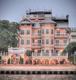 Un hotel de varios pisos con fachada rosa, balcones y vista al agua.