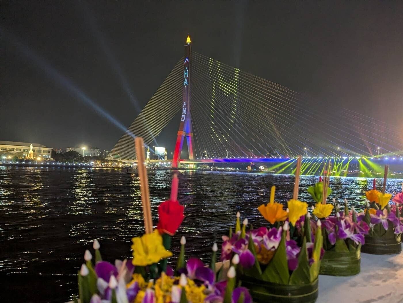 A nighttime view of a bridge with colorful lighting and a statue in the foreground.