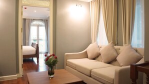 Un soggiorno con un divano color beige, un tavolino in legno e un vaso con fiori. Si intravede un letto con testata in legno sullo sfondo.