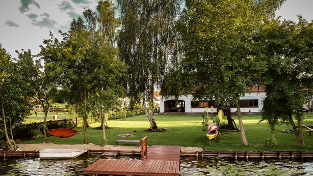 A wooden dock extending into a pond with lily pads, surrounded by lush greenery and a well-maintained lawn. - ApartView - Osada Zamkowa Pasym (Pasym)