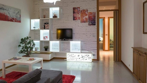 A modern living room with a white brick wall, a flat-screen TV, a white console table, and a red rug. - Casa Claudia (Montecassiano)