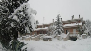 A snow-covered building with a brick facade, multiple chimneys, and a snow-covered roof. - Casa Claudia (Montecassiano)