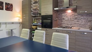 A modern kitchen with a dining table and chairs, built-in appliances, and a stone accent wall. - Casa Claudia (Montecassiano)