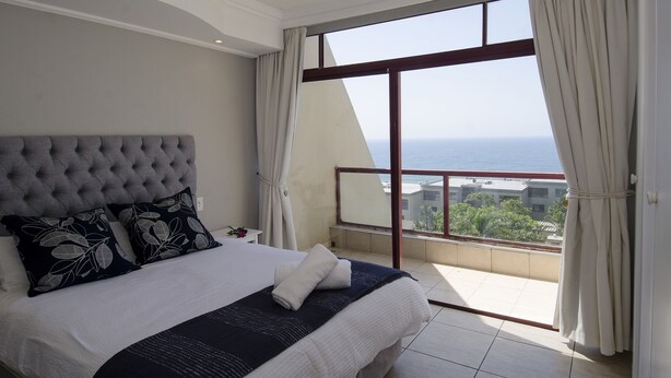 A bedroom with a large bed, a view of the sea, and a balcony with curtains. - C203 Surfside (eMdloti)