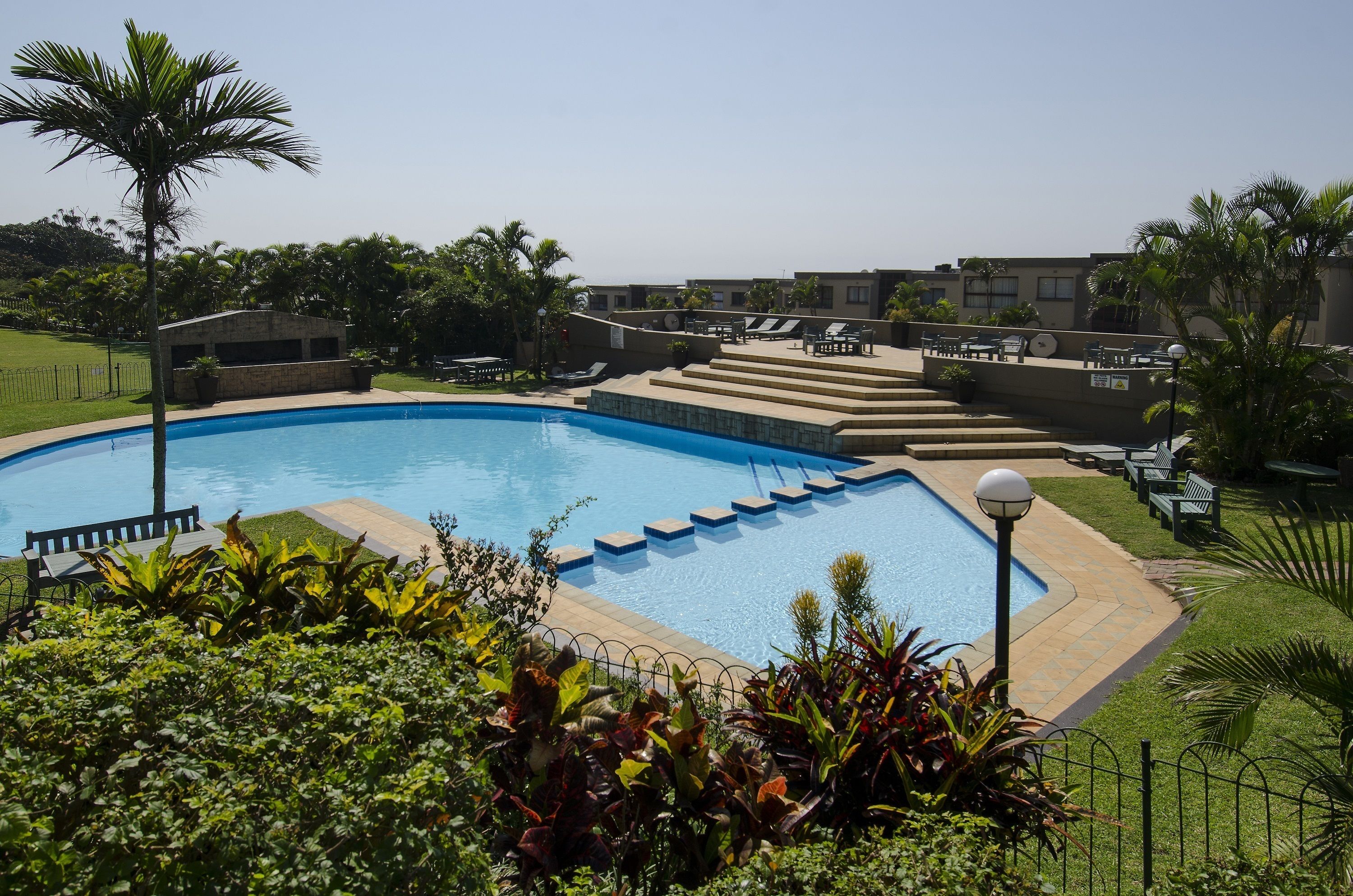 Una piscina con solárium, rodeada de vegetación y un cielo despejado.