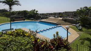 A swimming pool with a sun terrace, surrounded by greenery and a clear sky. - C203 Surfside (eMdloti)