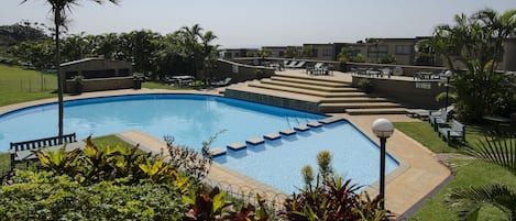 Una piscina con solárium, rodeada de vegetación y un cielo despejado.