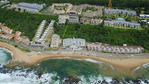 An aerial view of a coastal resort with multiple hotel buildings, a sandy beach, and a rocky shoreline. - C203 Surfside (eMdloti)
