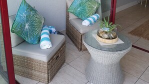 A balcony with wicker furniture, a glass table with a plant, and a view of the interior. - C203 Surfside (eMdloti)