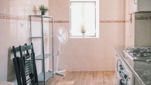 A kitchen with a gas stove, a fan, a window with a plant, and a shelf with a plant. - 03 Nice Flat by Travessa do Pasteleiro (Lisbon)