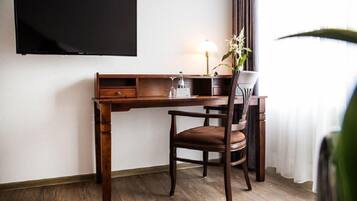 Un escritorio de madera con una silla, un televisor de pantalla plana montado en la pared, una lámpara y una planta en maceta.